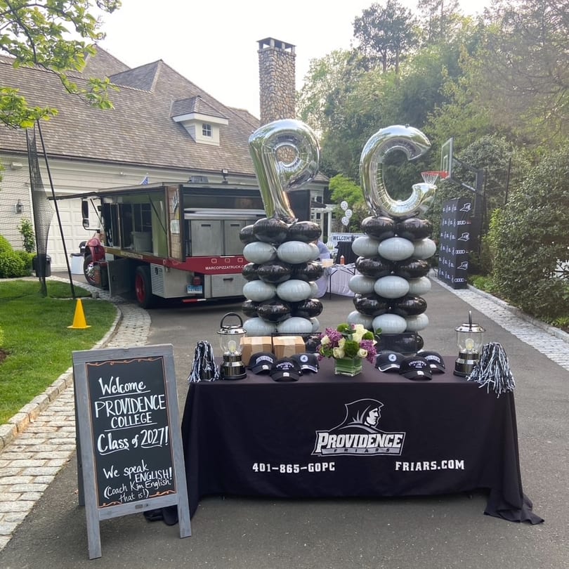Marco Pizzeria food truck parked next to a Providence College welcome table with balloons and merchandise.
