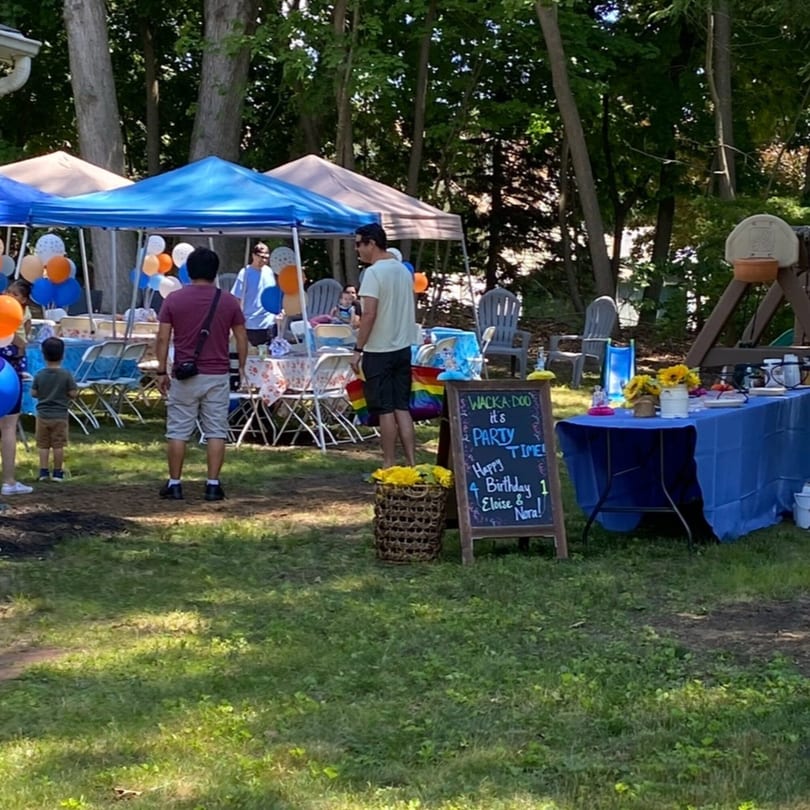 Outdoor birthday party with blue and orange balloons, tents, and a "Party Time" sign.