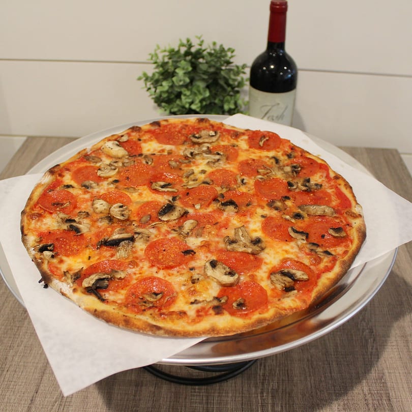 Marco Pizzeria's pepperoni and mushroom pizza on a metal tray with a bottle of wine and plant in the background.