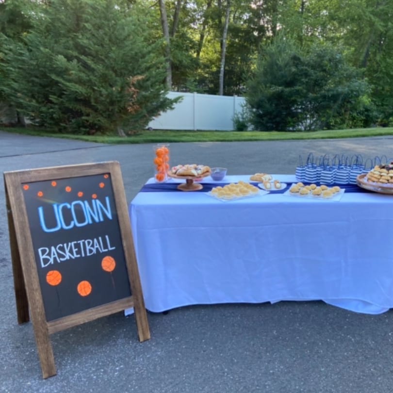 Outdoor table with blue tablecloth, desserts, and a chalkboard sign for "UCONN BASKETBALL".