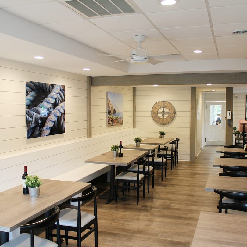 Bright, modern dining room at Marco Pizzeria with light wood tables, black chairs, and nautical decor.