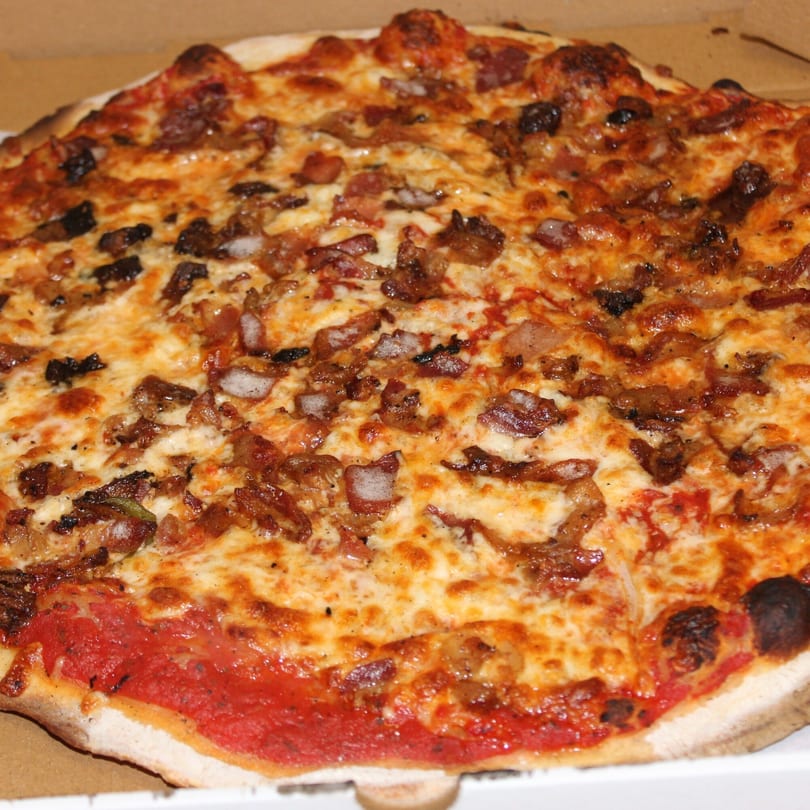 A close-up of a Marco Pizzeria pizza with melted cheese, bacon, and caramelized onions.