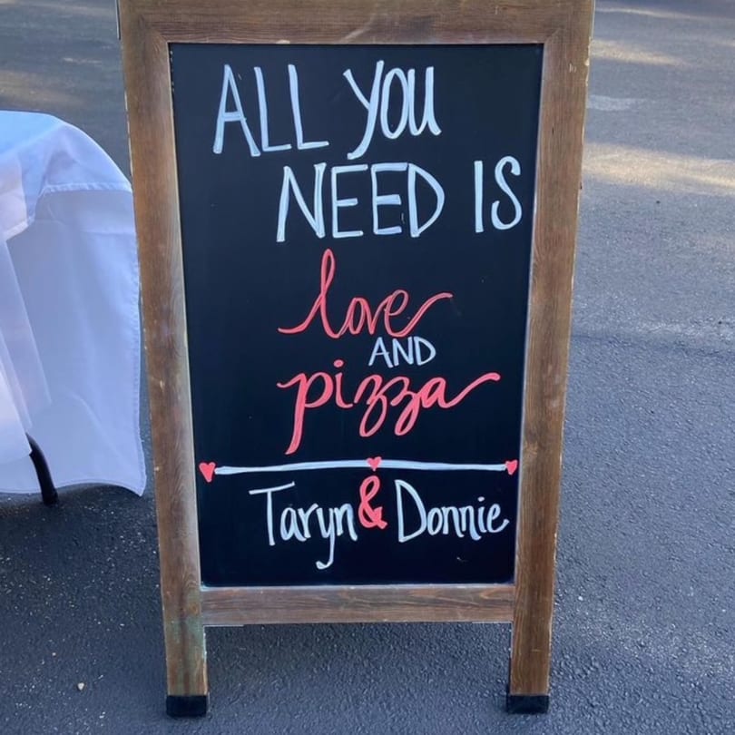 A chalkboard sign reads "ALL YOU NEED IS love AND pizza Taryn & Donnie" in white and pink.
