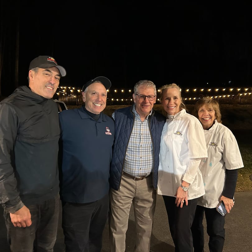 Five smiling people, including two women in Marco Pizza Truck chef coats, stand together at night.