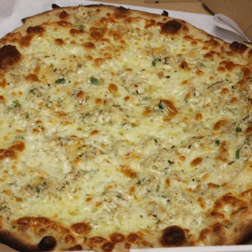 A close-up of a white pizza from Marco Pizzeria, topped with melted cheese and herbs.