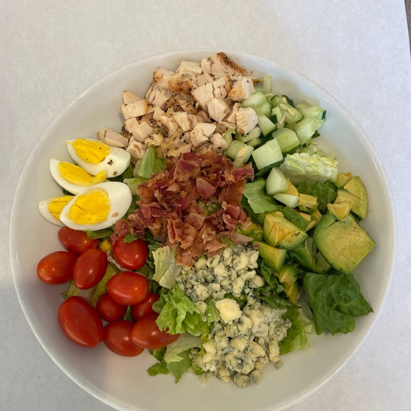 A vibrant Cobb salad with chicken, bacon, eggs, tomatoes, avocado, cucumber, and blue cheese.
