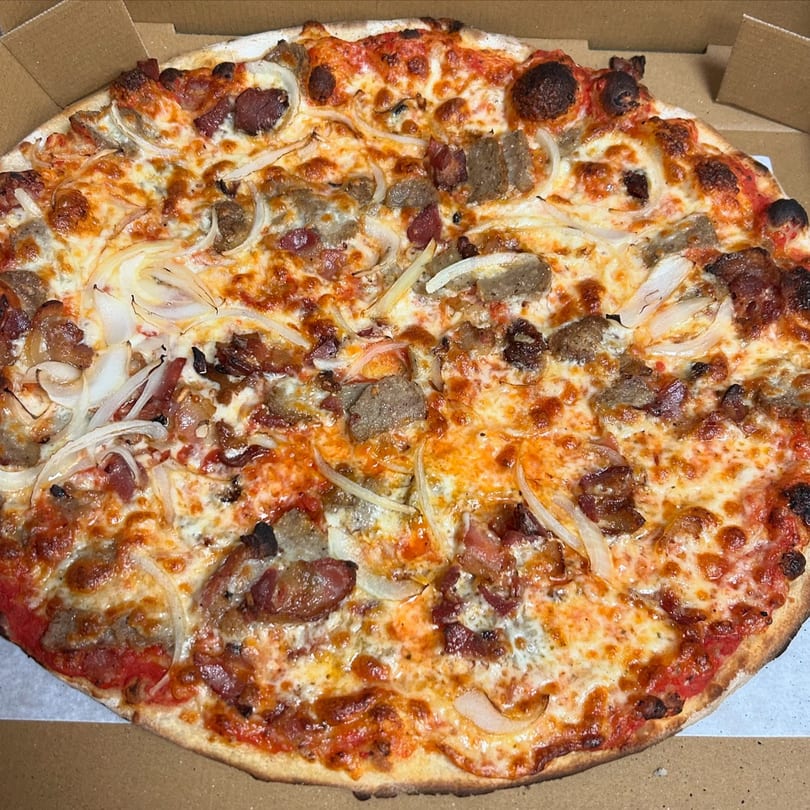 A Marco Pizzeria pizza with sausage, bacon, and onions in a cardboard box.
