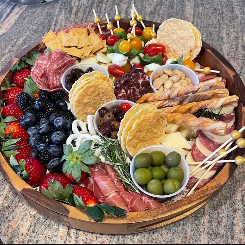 A large wooden charcuterie board filled with Italian meats, cheeses, berries, olives, and crackers.