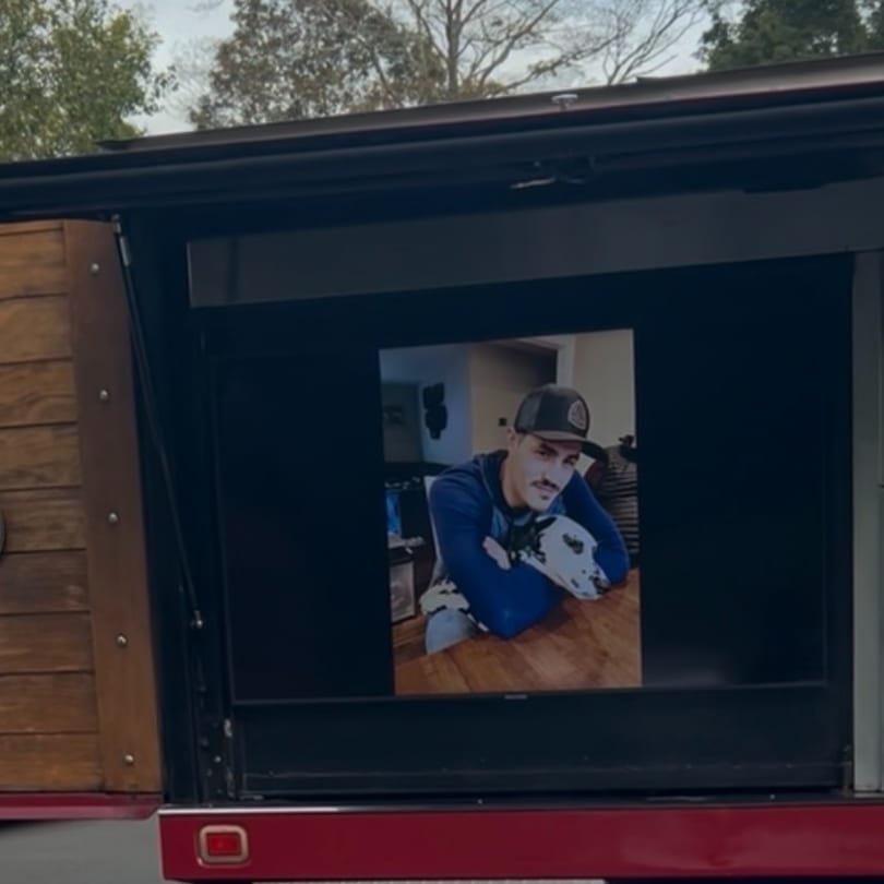 A man in a baseball cap and blue shirt with a dalmatian dog on a wooden table.