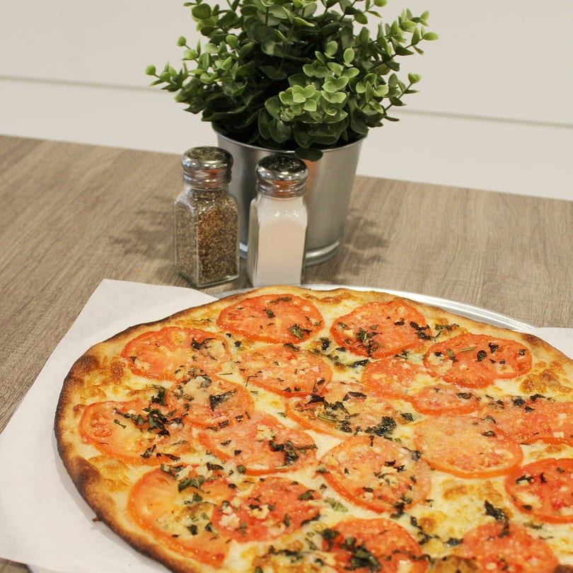 A Marco Pizzeria Margherita pizza with sliced tomatoes and basil, next to salt and pepper shakers.