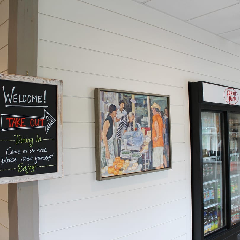 Chalkboard sign with "Welcome! Take Out Dining In" next to a painting and a beverage cooler.