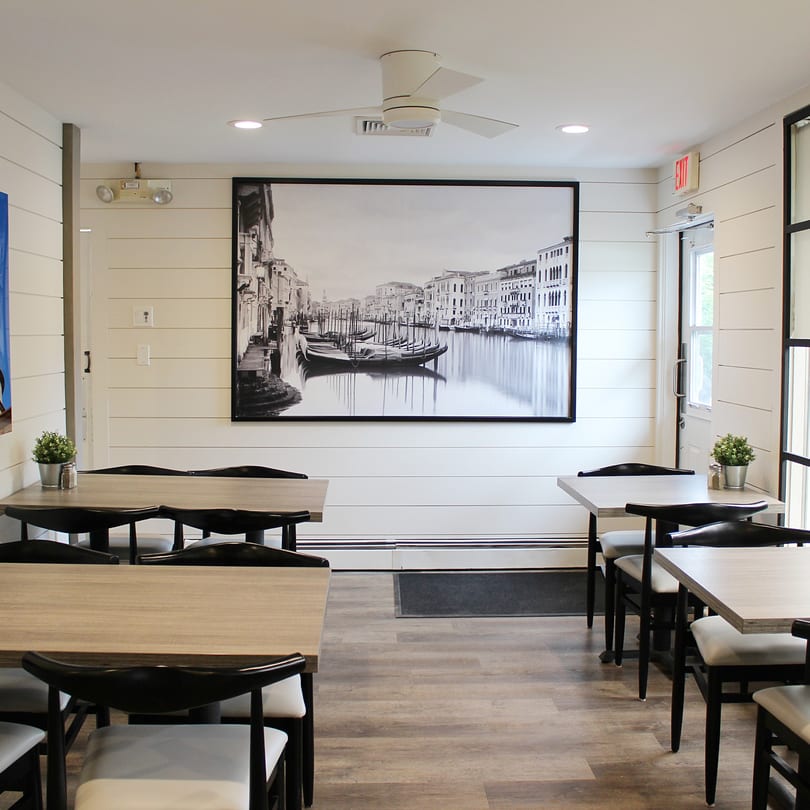 Marco Pizzeria's dining room with light wood tables, black chairs, and a large Venice canal mural.