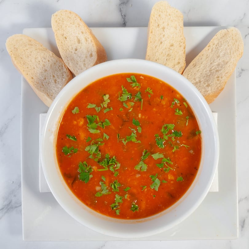 A white bowl of Marco Pizzeria's minestrone soup with parsley and four slices of bread.