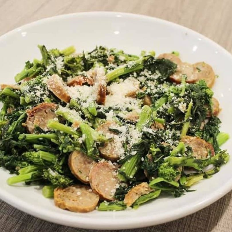 Marco Pizzeria's broccoli rabe and sausage dish, topped with grated cheese in a white bowl.