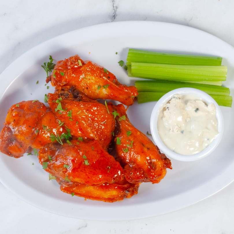 Marco Pizzeria's buffalo wings, with celery sticks and blue cheese dressing on a white plate.