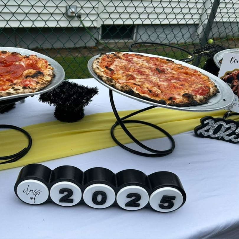 Two Marco Pizzeria pizzas on stands, a pepperoni and a cheese, with "Class of 2025" decor.