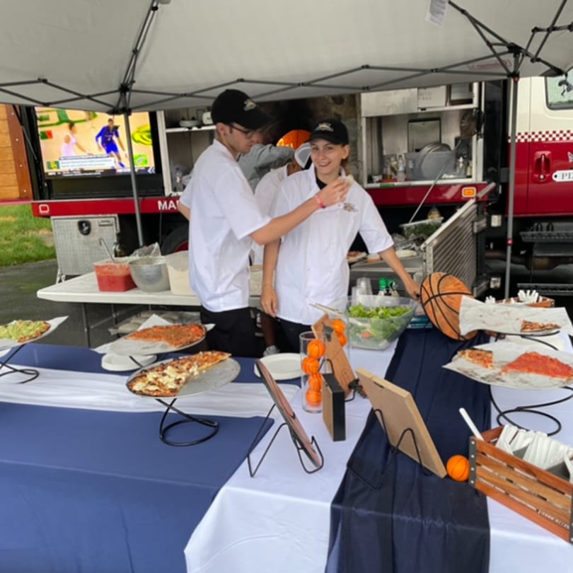 Marco Pizzeria staff serving pizzas and salad from a food truck at an outdoor event.