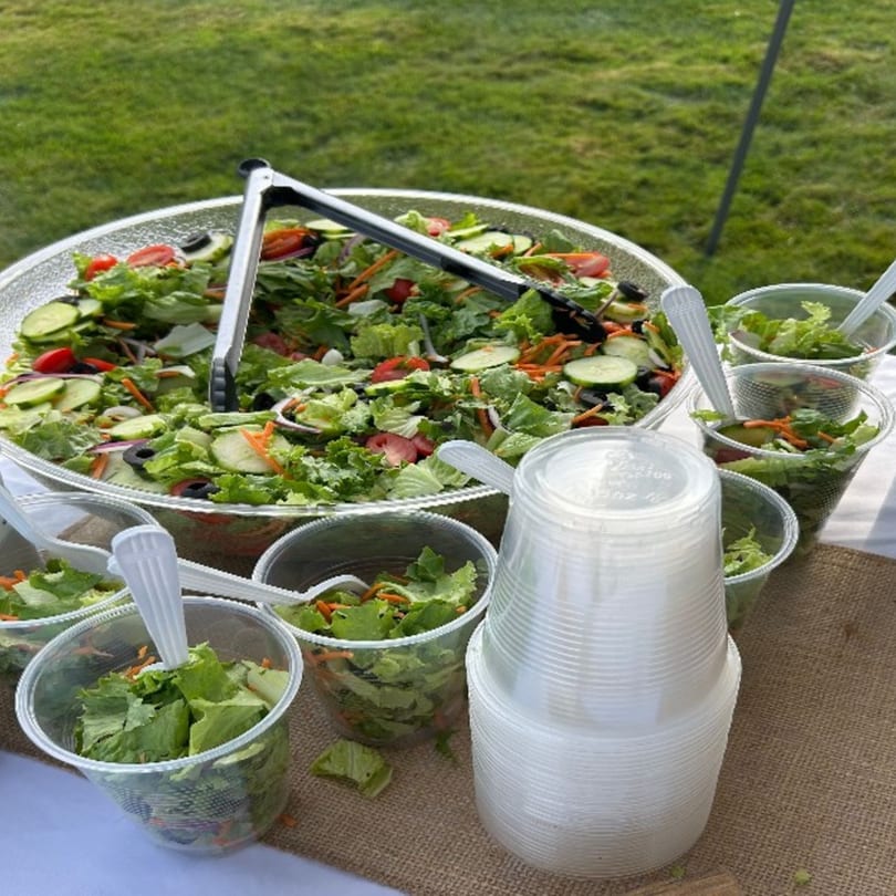 Large bowl of garden salad with individual plastic cups of salad and a stack of empty cups.