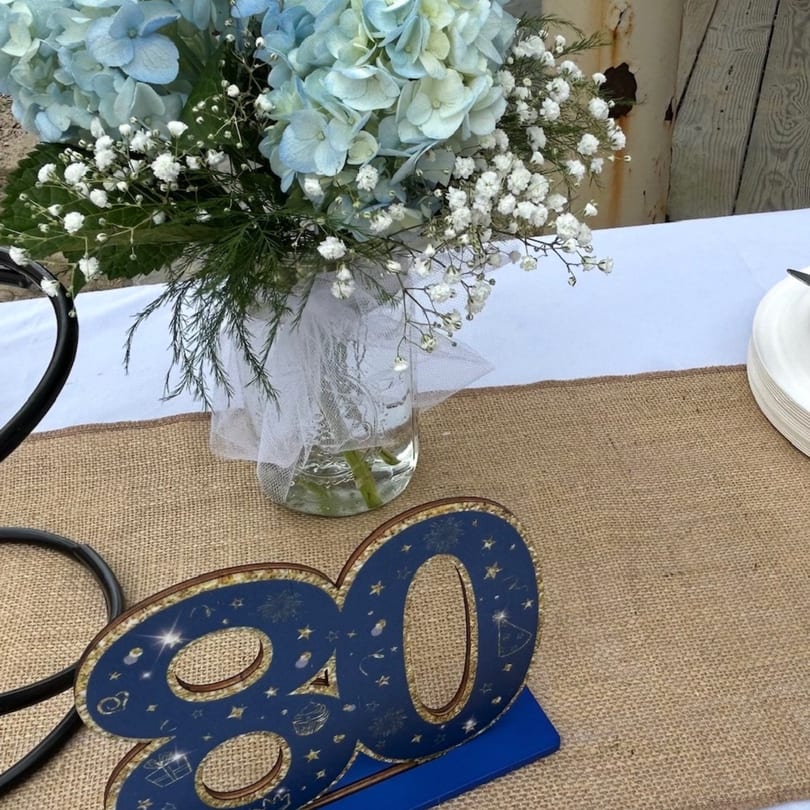 Table setting with a blue hydrangea centerpiece, a burlap runner, and a blue '80' decoration.